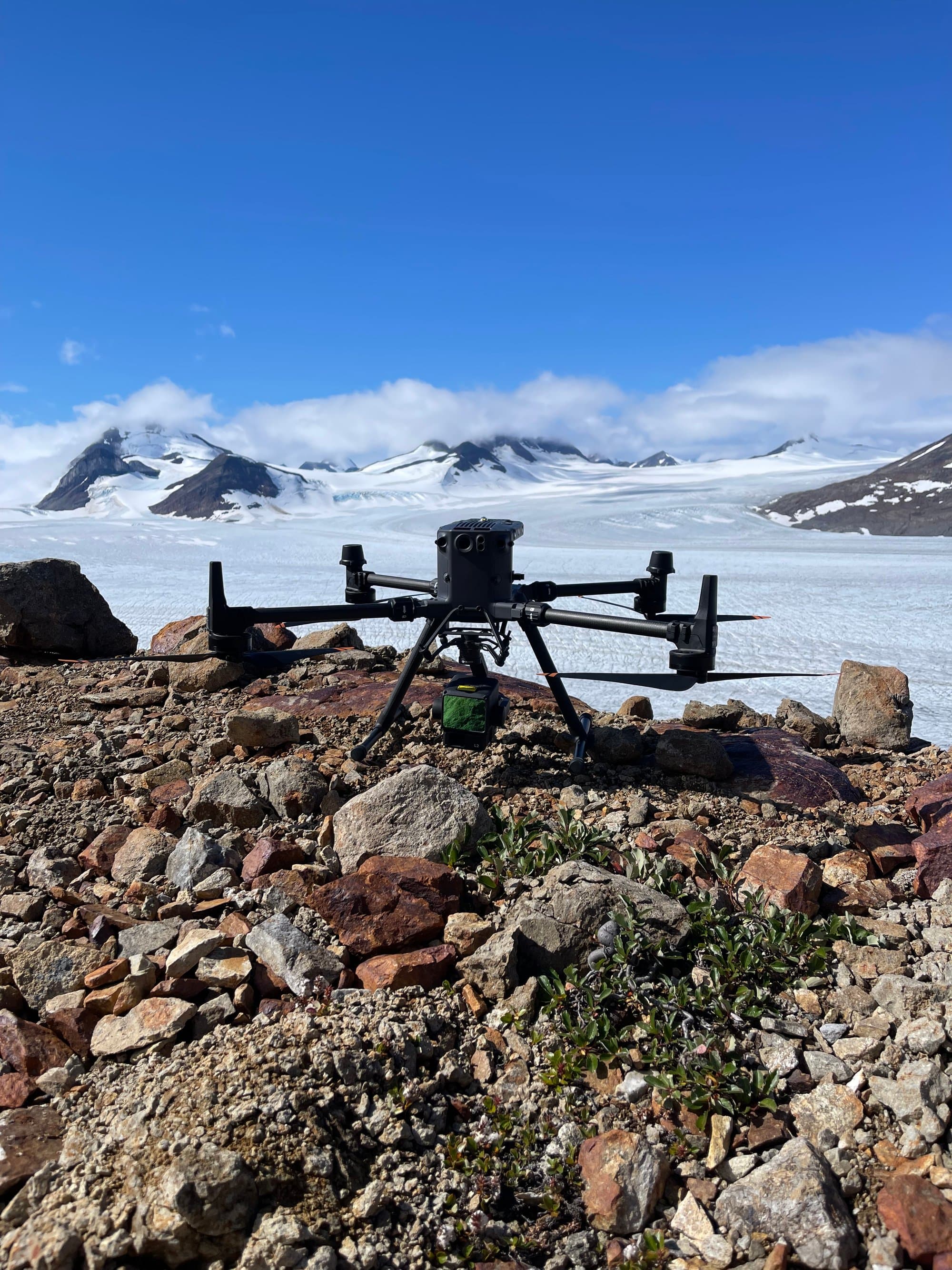 DJI M300 drone with LiDAR sensor staged on a rocky ridge above a glacier