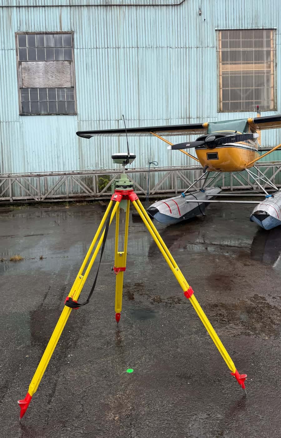 GNSS base station on a survey tripod beside a floatplane on a wet apron at a remote northern site