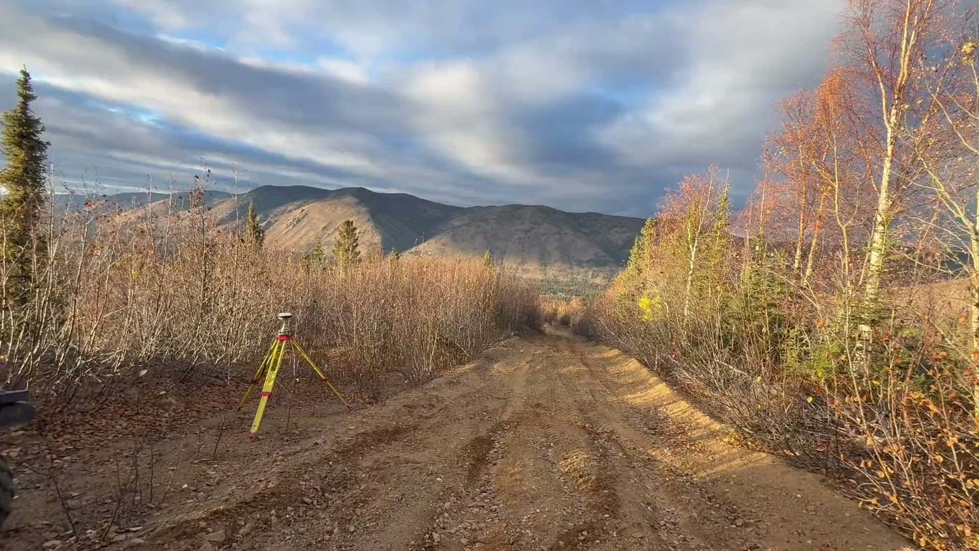 GNSS survey base station on a tripod beside an ATV on a backcountry access trail in fall