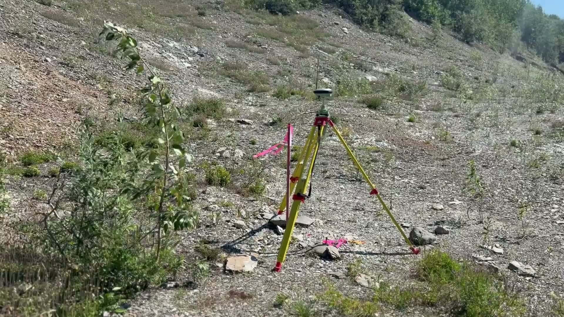 GNSS survey base station on a yellow tripod with flagging on a rocky mine site slope in summer
