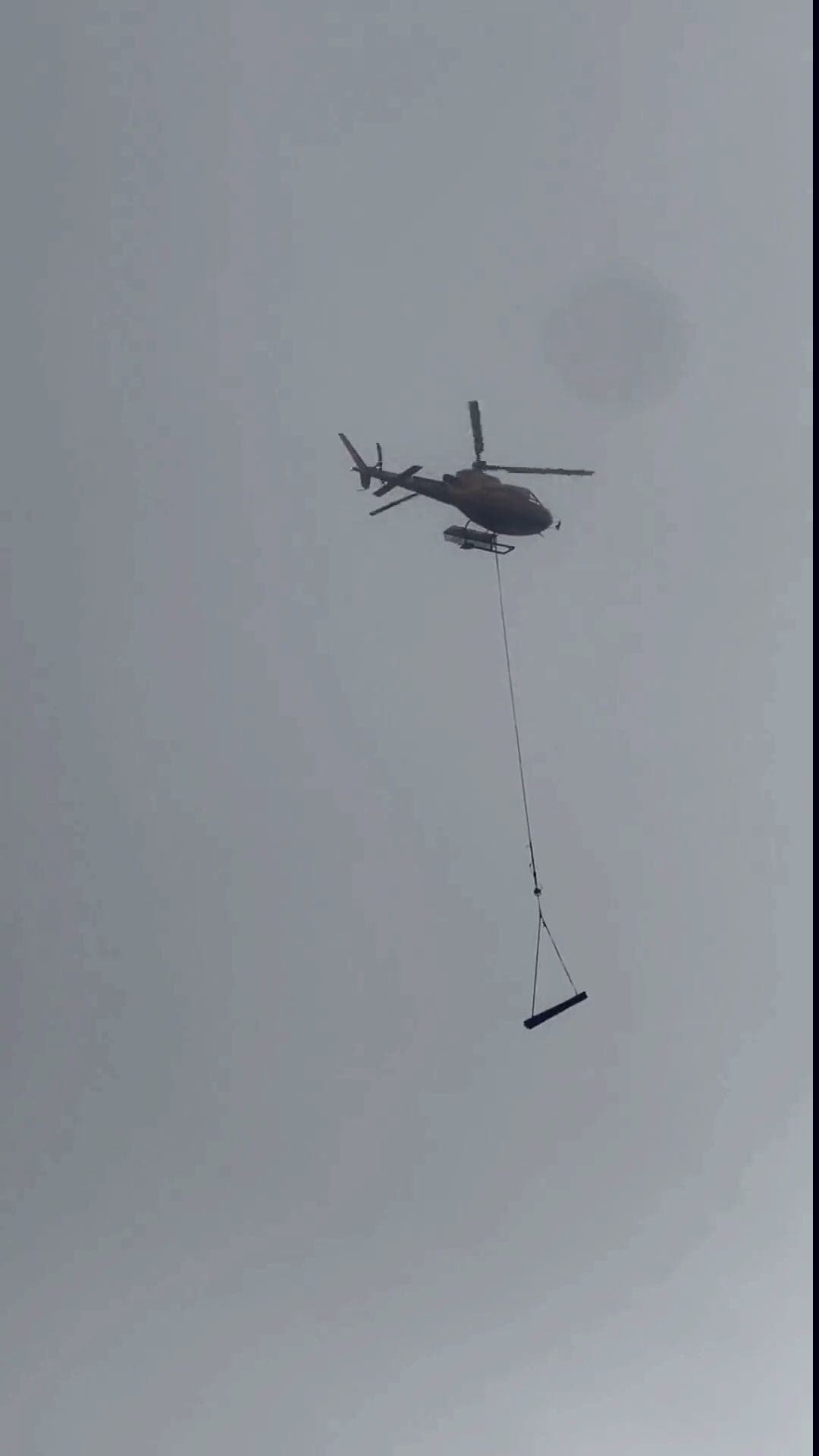 Helicopter longlining equipment onto a glacier moraine survey site in alpine fog