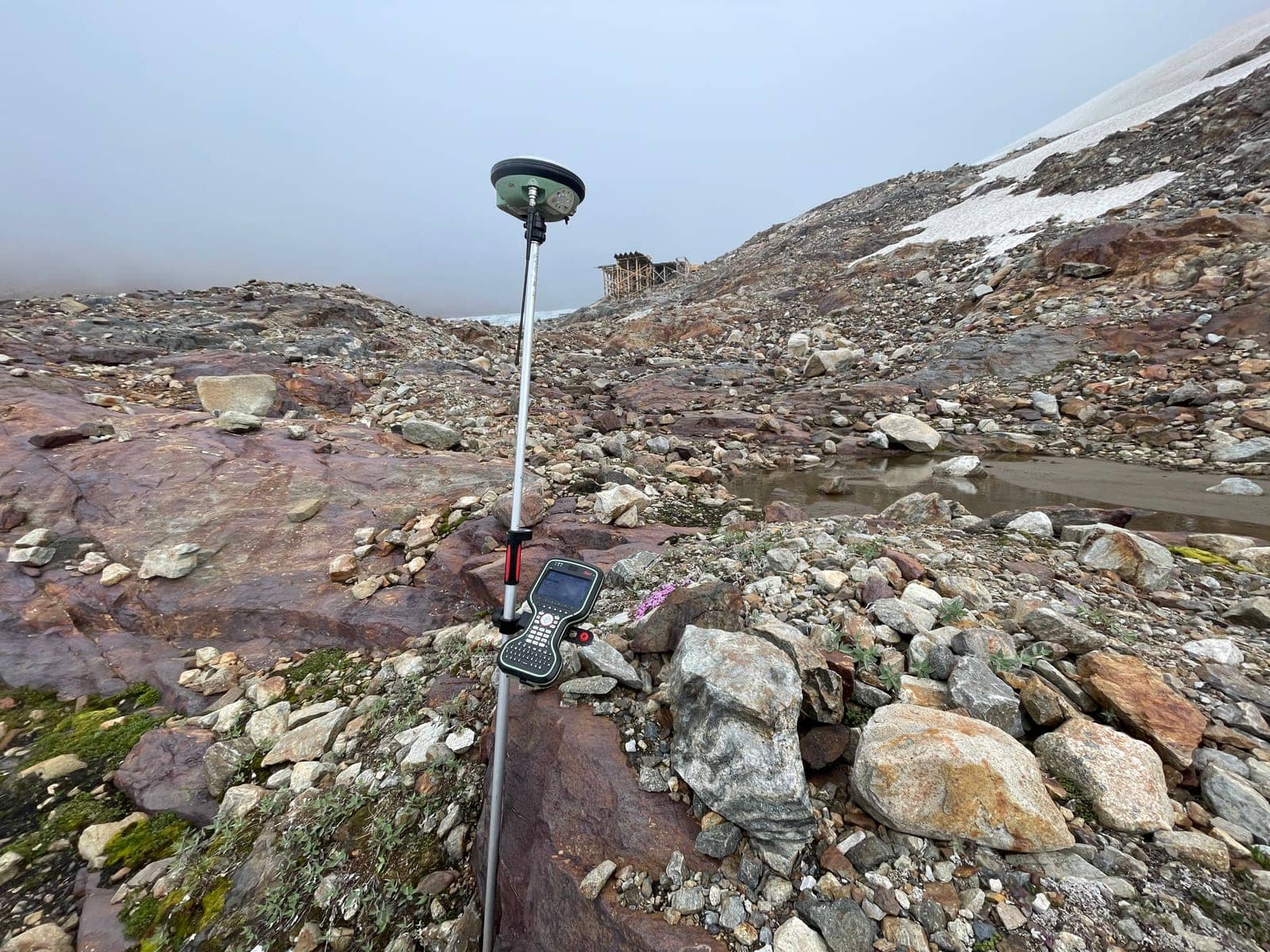 GNSS rover set up on rocky alpine ground below historic wooden mine workings