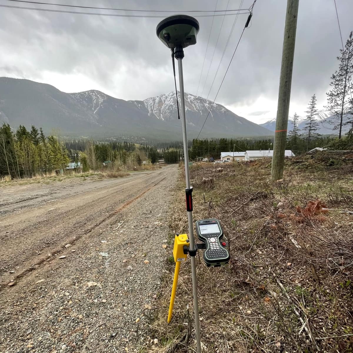 GNSS rover on a gravel road in a northern valley with snow-covered peaks behind