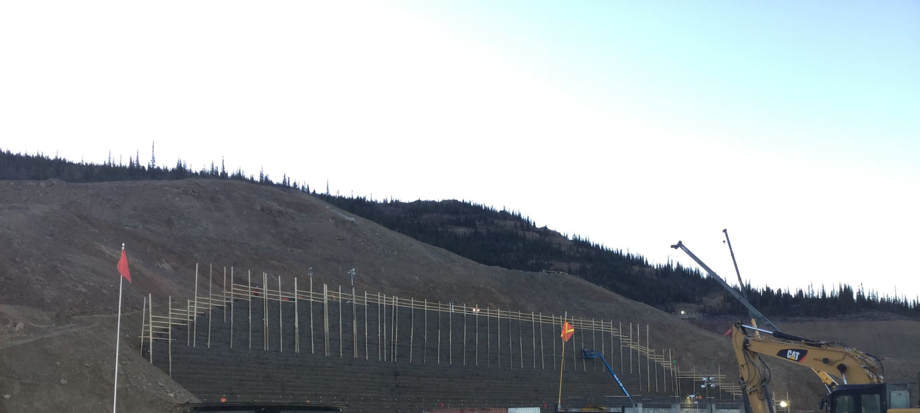 Tiered retaining wall under construction at a mine site, with layout rods standing along the face