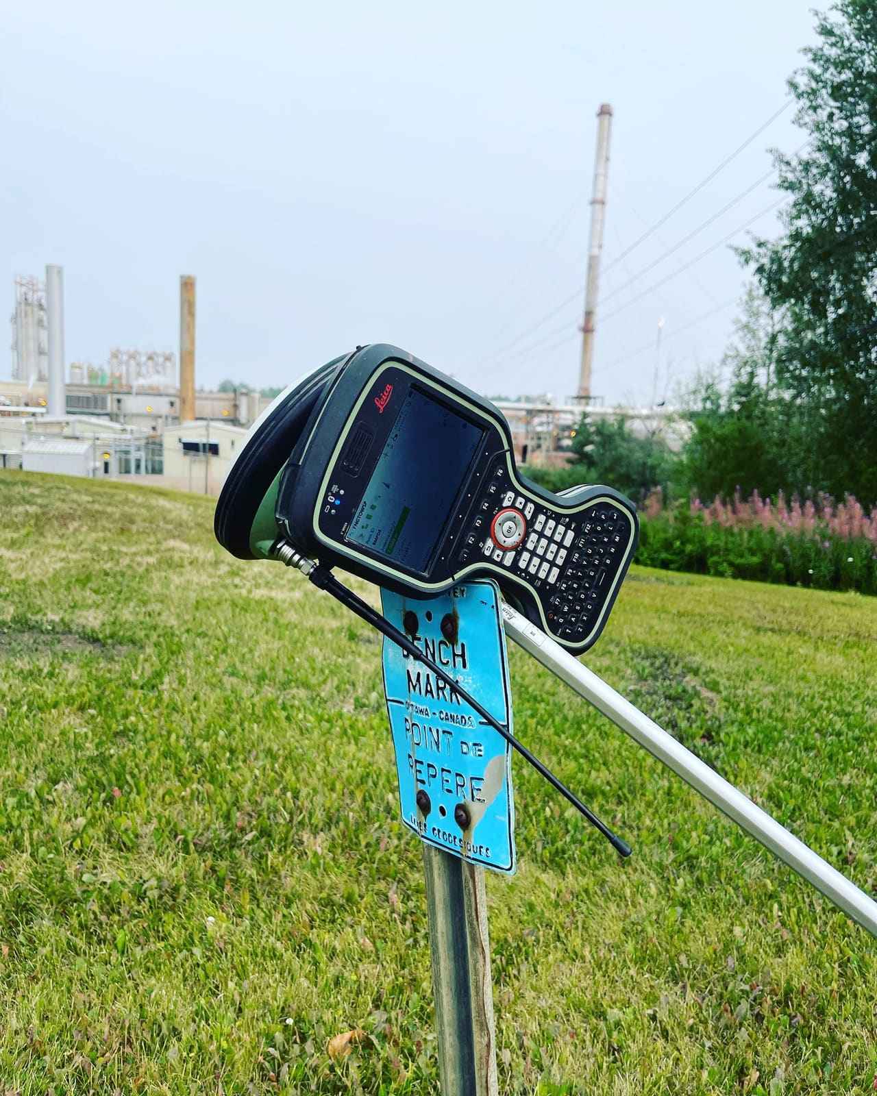 Survey field controller resting on a bench mark plate beside the rover pole