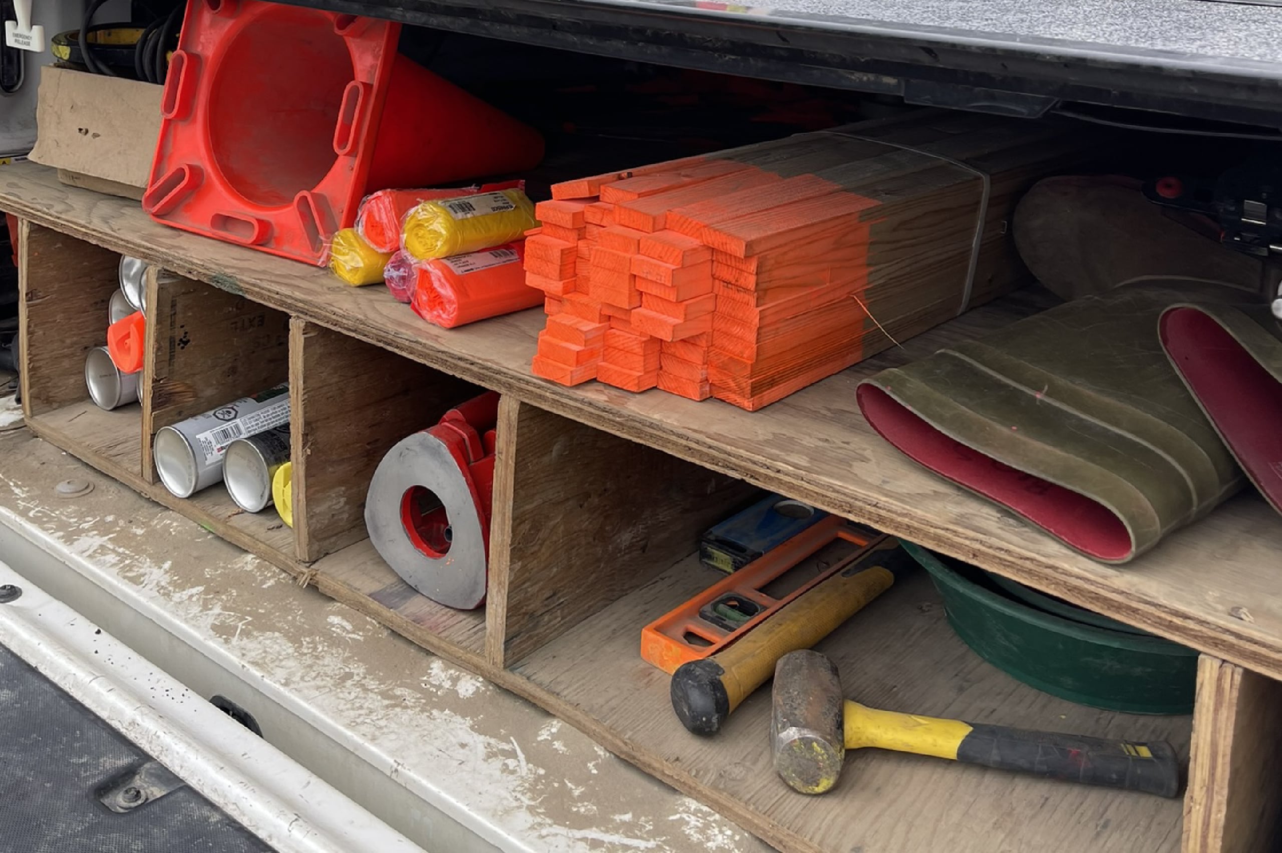 PCI's surveying tools and equipment stored in a truck bed, including wooden stakes, marking flags, traffic cones, hammer, level, and other field essentials.