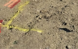 Utility locating markings and coloured flags on a construction site for drilling and excavation showing red, yellow, and orange lines and markers. Yellow is gas, orange is telephone and red is power/electric.